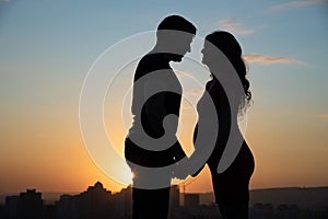 Silhouettes of a pregnant woman and her husband on the background of a beautiful sunset