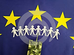 Silhouettes of refugees from paper fleeing military aggression against background of EU flag