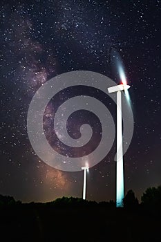 silhouettes of the rotating blades of a windmill propeller against the night sky with milky way. Wind energy production. Clean