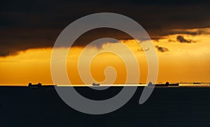 Silhouettes of ships at sea against a bright sunset sky, sunlight reflected from the waves, dramatic sky