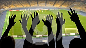 Silhouettes of soccer fans hands during match, crowded football stadium, sport