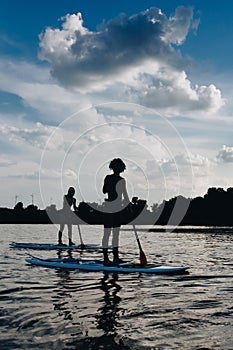 silhouettes of sportswomen surfing on paddleboards on river