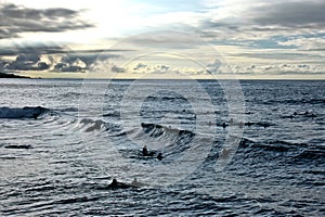 Silhouettes of surfers in the Atlantic Ocean waiting for a wave as the sun sets in the background