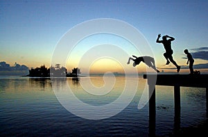SILHOUETTES OF TEENAGERS JUMPING FROM A PONTOON INTO THE WATER WITH A FANTASTIC SKY BACKGROUND AT SUNSET. OUDOORS, PEOPLE