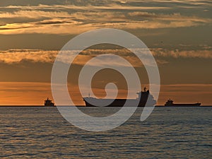 Silhouettes of three cargo vessels mooring in English Bay in front of Vancouver, Canada at sunset with orange dramatic sky.