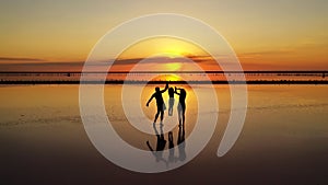 Silhouettes of three, dad, mom and little daughter walking through the shallows of a lake against the background of a red-orange