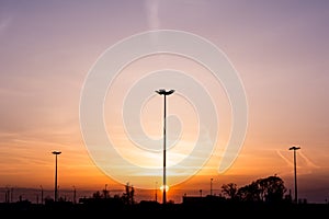 Silhouettes of three lampposts of street lighting form a perspective of a triangle against the sunset over the horizon