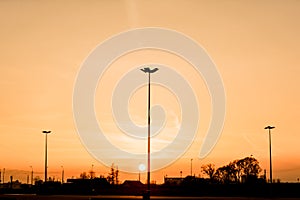 Silhouettes of three lampposts of street lighting form a perspective of a triangle against the sunset over the horizon