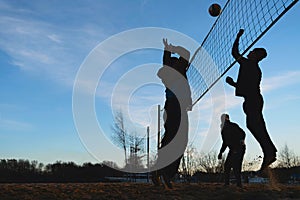 Silhouettes of three men playing beach volleyball
