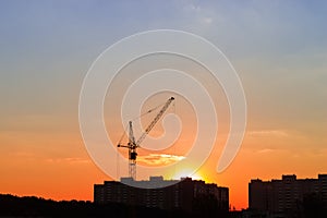 Silhouettes of tower crane and building under construction during sunset