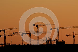 Silhouettes of tower cranes against the background of the setting sun