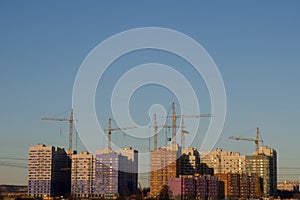 Silhouettes of tower cranes against of residential houses in the microdistrict. Industrial skyline view of the construction