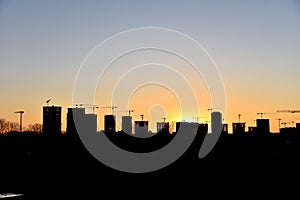 Silhouettes of tower cranes and builders in action on sunset background. Workers during formwork and pouring concrete through a Ñ
