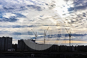 Silhouettes of tower cranes and buildings under construction on the background of the sunset sky. Back light. Large construction