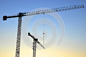 Silhouettes of tower cranes constructing a new residential building at a construction site against sunset background. Renovation