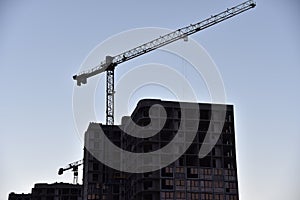 Silhouettes of tower cranes constructing a new residential building at a construction site on sunset background. Crane lifting a