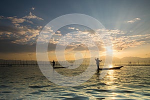 Silhouettes of the traditional fishermen throwing fishing net du