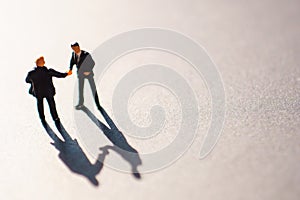 Silhouettes of two businessman, probably men, shaking their hands as a sign of an agreement or deal. The meeting takes place on