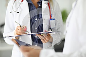 Silhouettes of two doctors in white coats one holding clipboard with pen, the second tablet.