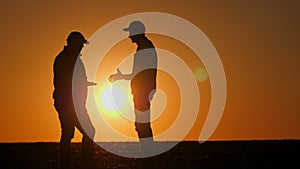 Silhouettes of two farmers shaking hands against the sky where the sun sets