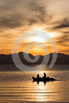 Silhouettes of two men in boat at sunrise in Corfu