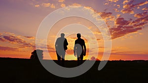 Silhouettes of two men - son and father go together to meet the sunset. Back view. Steadicam shot