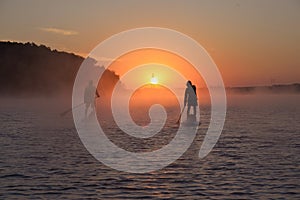 Silhouettes of two men on SUP boards against the background of the rising sun