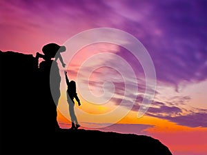 Silhouettes of two people climbing on mountain and helping