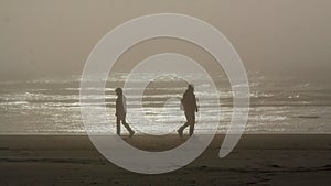 Silhouettes of two persons walking in an opposite directions on a Tillamook beach, Oregon