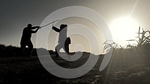 silhouettes of two samurai fighting with swords in the rays of sunset