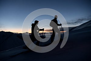 Silhouettes of two skiers with flashlights on their foreheads climbing the mountain slope