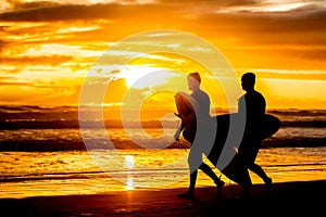 Silhouettes of two surfboarders with boards walking by beach at