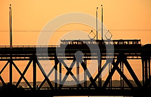 Silhouettes of a two-tiered bridge and 2 trams on a sunset background