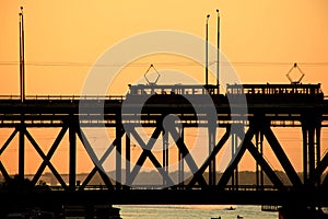 Silhouettes of a two-tiered bridge and 2 trams on a sunset background