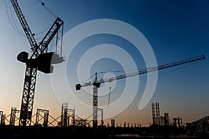 Silhouettes of two tower cranes on the construction site