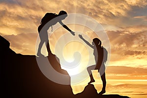 Silhouettes of two women climber climb the mountain helping each other