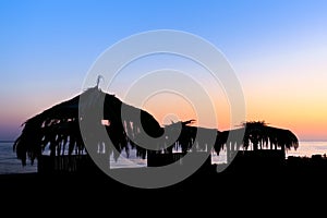 Silhouettes of wooden hovels covered with reeds and palm leaves on the beach at sunset