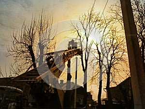 Silhouettes of workers pruning tall trees with an aerial work platform in the golden rays of the sun. The concept of work on the