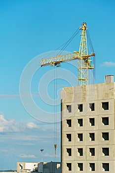 Silhouettes of working construction cranes against the background of an unfinished residential building. Multi-storey luxury