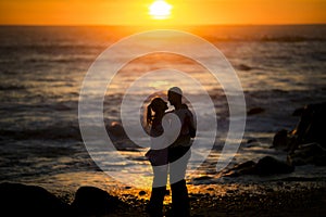 Silhouettes of a young couple in a cuddle position on the beach during a golden sunset.