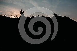 Silhouettes of a young couple lovers at sunset on dramatic sky background. Place for text or advertising