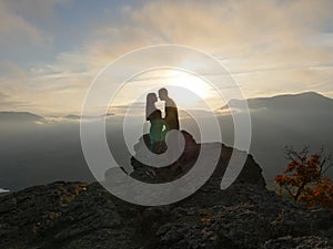 Silhouettes of young couple standing on a mountain and looking to each other on beautiful sunset background. Love of guy