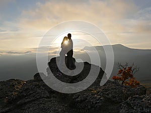 Silhouettes of young couple standing on a mountain and looking to each other on beautiful sunset background. Love of guy