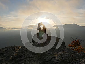 Silhouettes of young couple standing on a mountain and looking to each other on beautiful sunset background. Love of guy