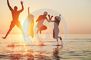 Silhouettes of young friends having fun in water for beach party - Group of happy people dancing and jumping inside sea on