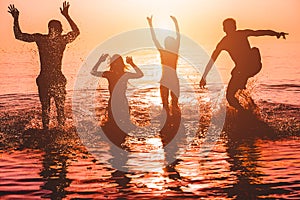 Silhouettes of young friends having fun in water for beach party - Group of happy people dancing and jumping inside sea on