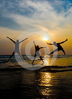 Silhouettes of young group of people jumping on the beach at sun