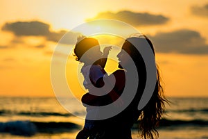 Silhouettes young mother with daughter playing and smiling on the beach at sunset. Happy family and travel concept.