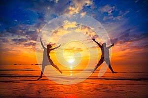 Silhouettes of young people jumping at sunset on the sea beach. Happy.