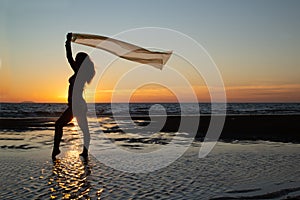 Silhoutte of a pretty senior Asian female in a swimming suit standing and flaunt yellow fabric on the beach.